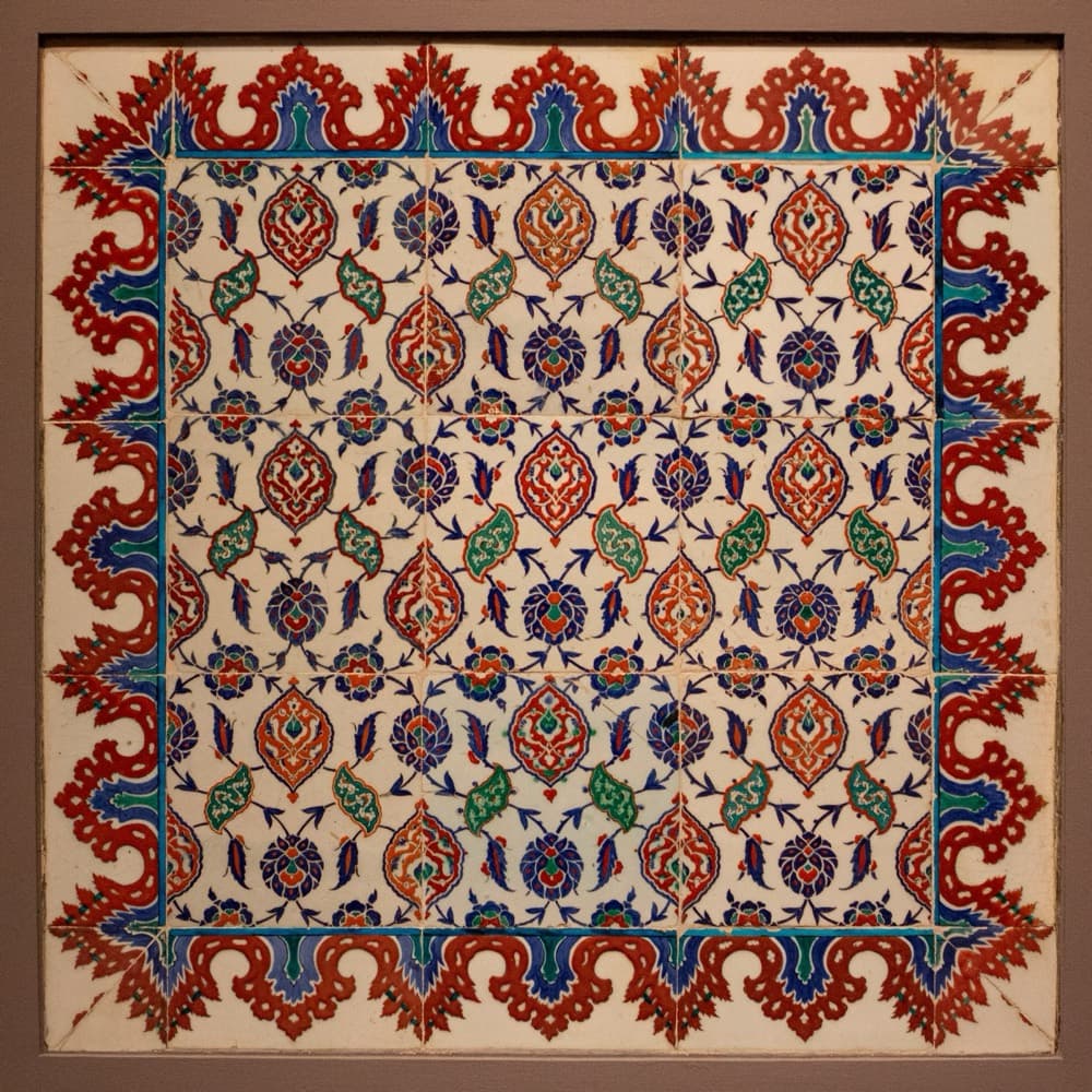 Tile panel with a red wavy border: red medallions, green saz leaves and cobalt-blue flowers on white.